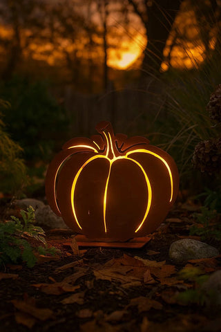 Carved pumpkin with glowing interior in a natural setting during sunset.