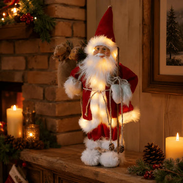 Large Father Christmas figure in a red coat holding a lantern in a cosy fireside Christmas display.